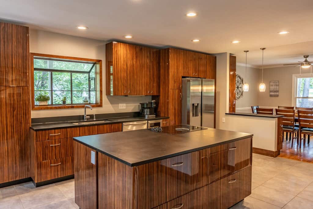 A contemporary kitchen featuring wood-paneled cabinets, a central island, stainless steel appliances, and a view into the dining area.