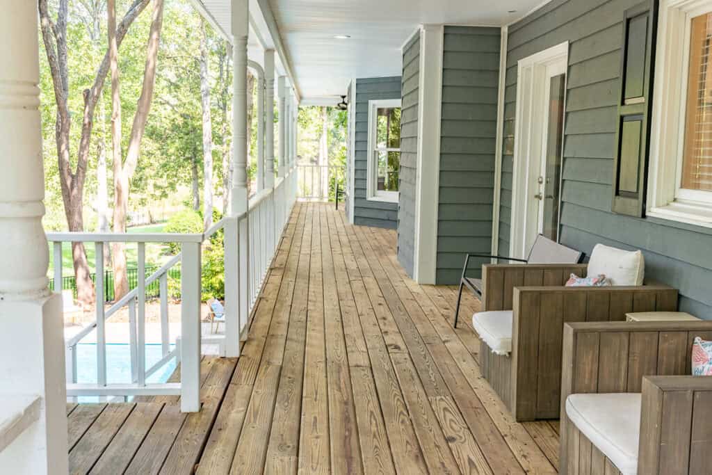 A cozy section of the wraparound porch with wooden lounge chairs and cushions, set against a backdrop of trees.