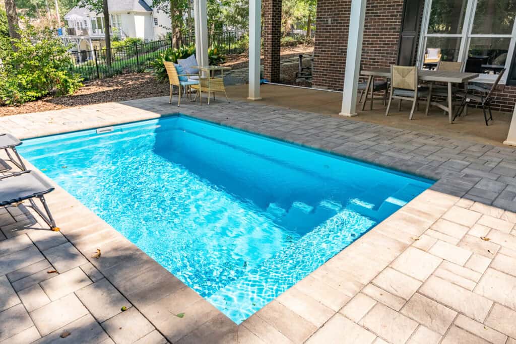A poolside patio area with loungers and dining space, surrounded by greenery.
