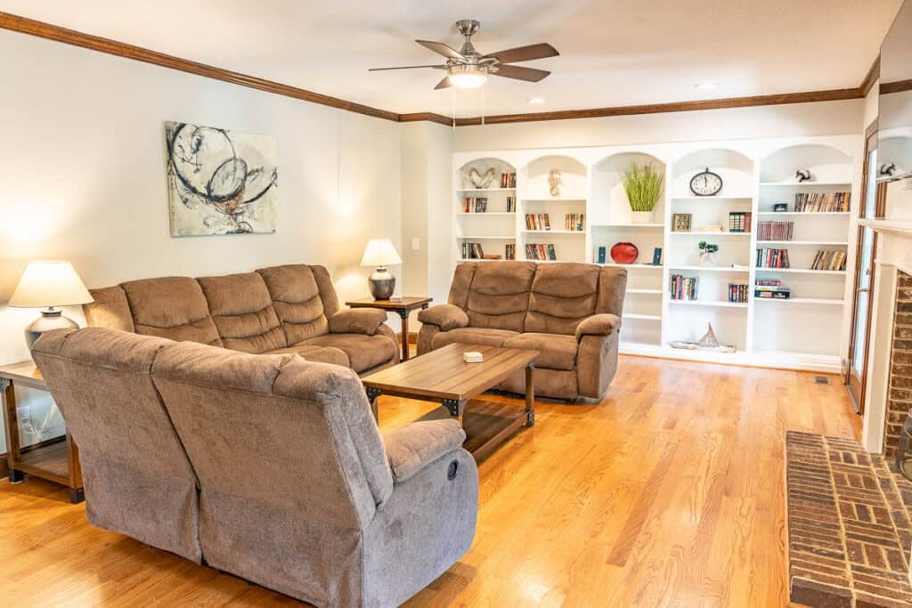 A comfortable living room with plush reclining sofas, built-in bookshelves, and warm lighting. The space exudes a welcoming ambiance, perfect for relaxation or entertaining.